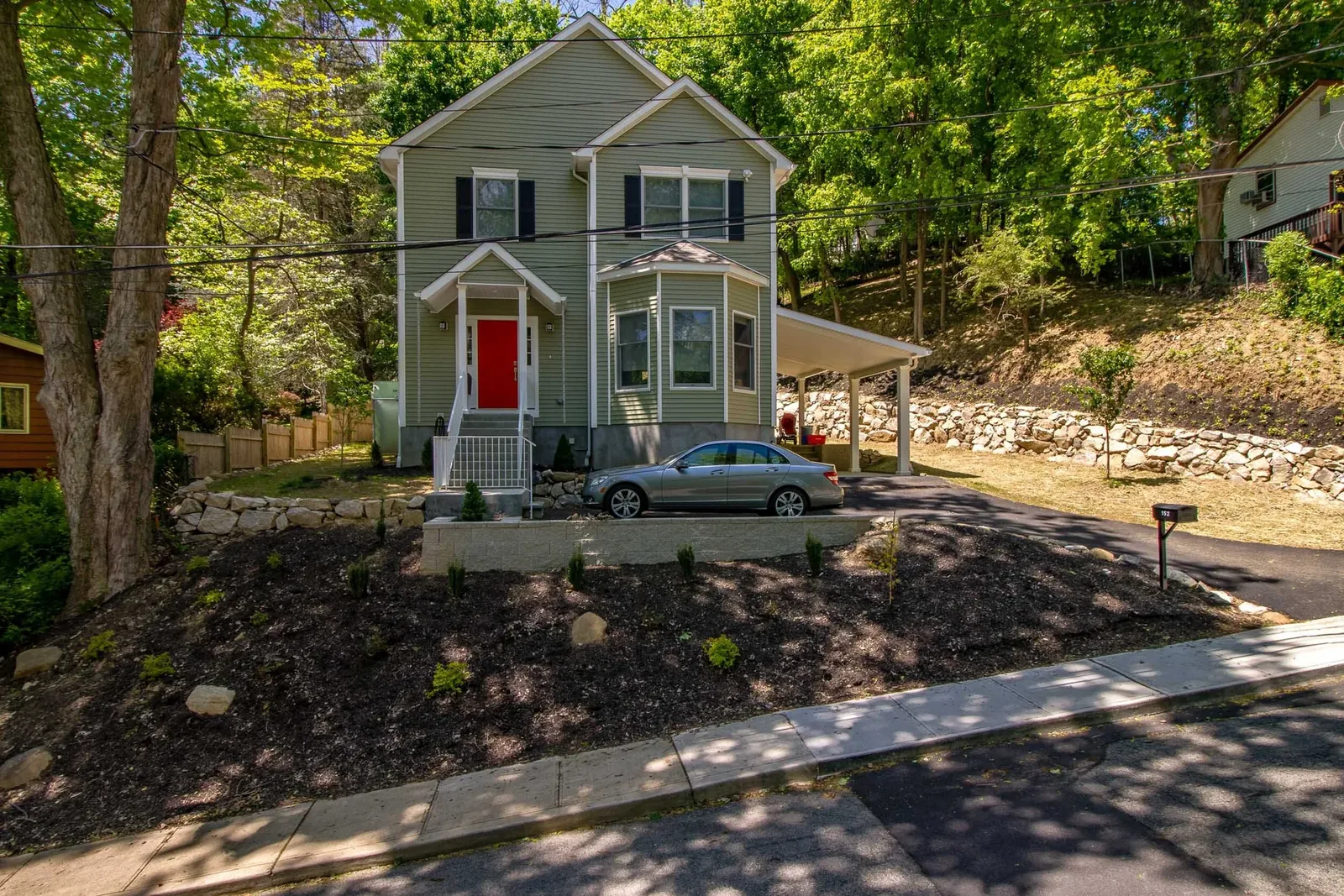 Green home with red door, bay window, and carport