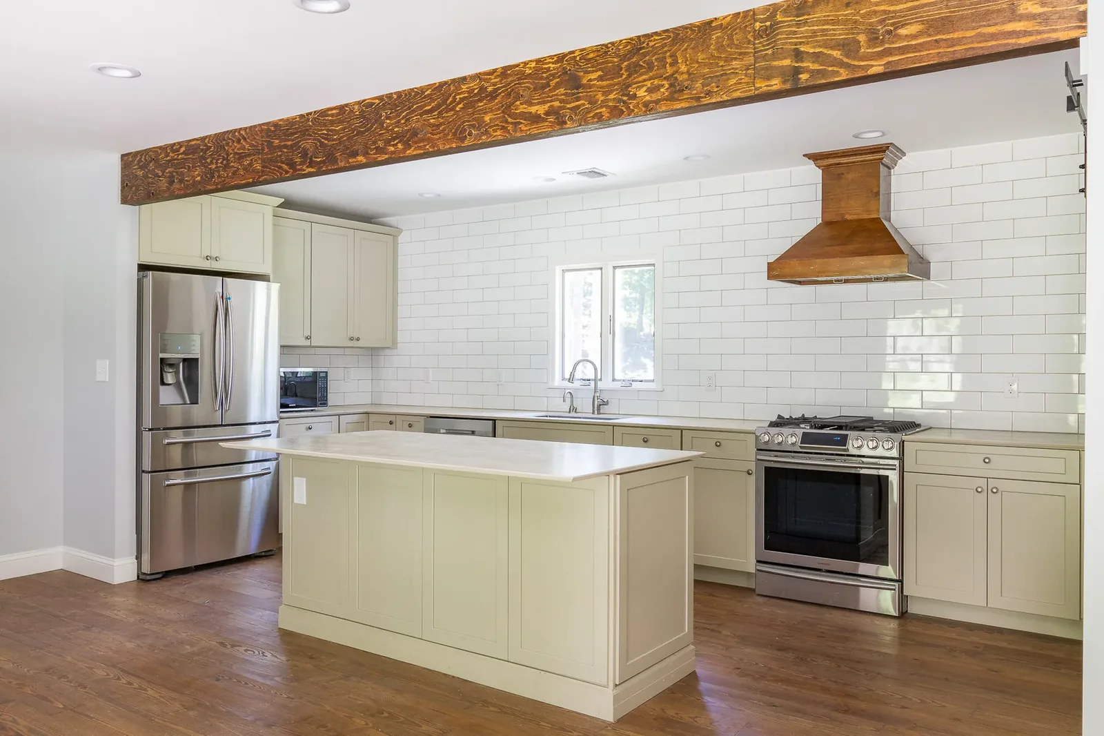 Sage kitchen with wood beam, island, and wood range hood
