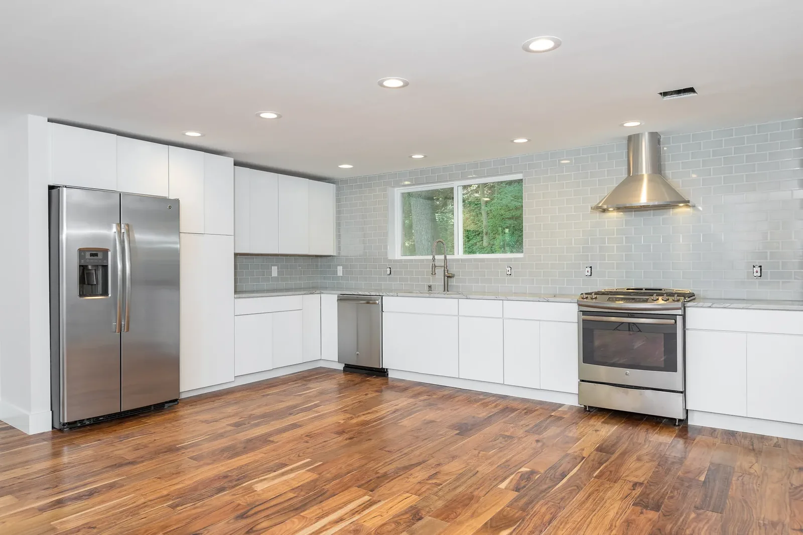 White kitchen with glass tile backsplash and stainless hood