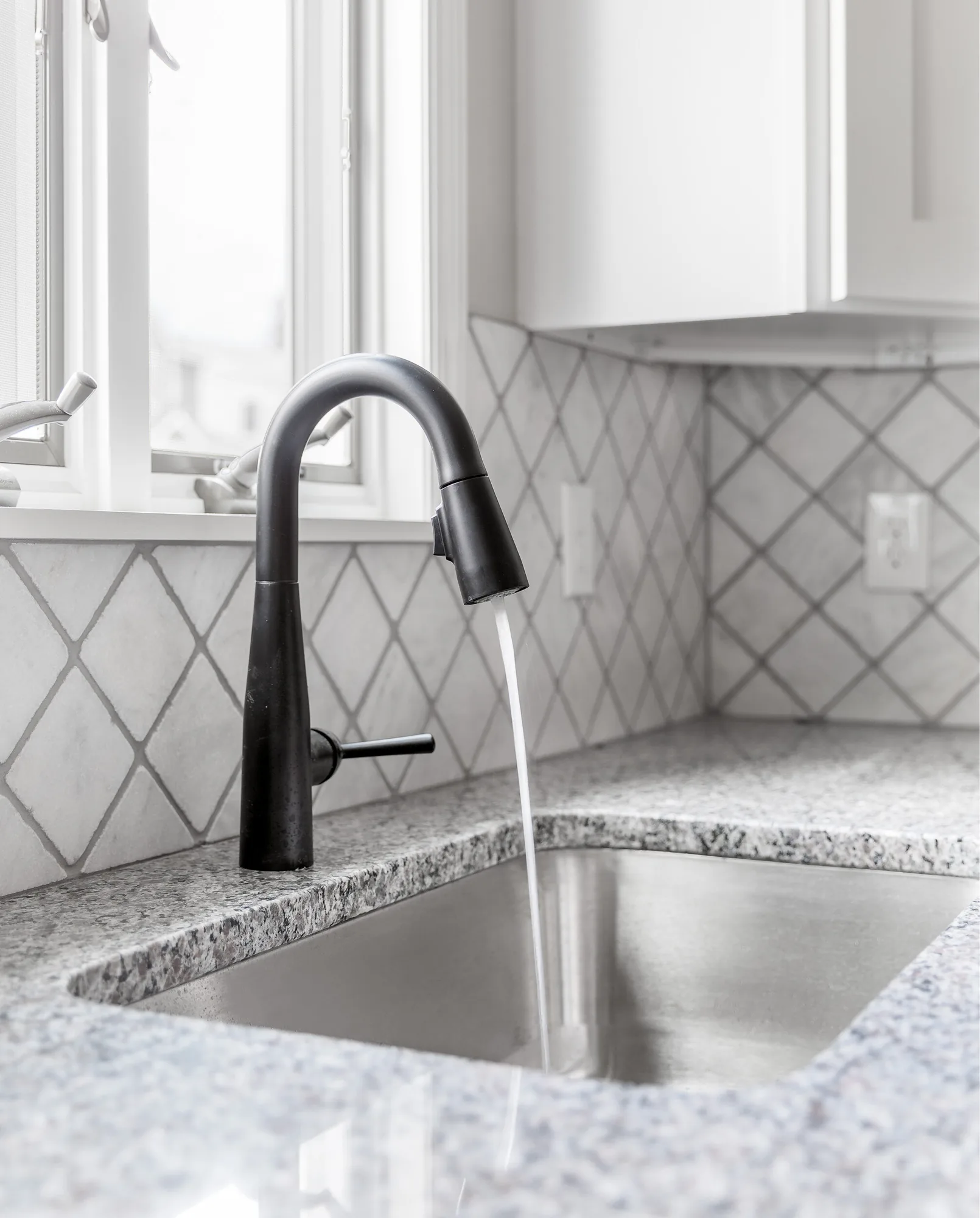 Matte black faucet over a stainless sink with marble diamond backsplash