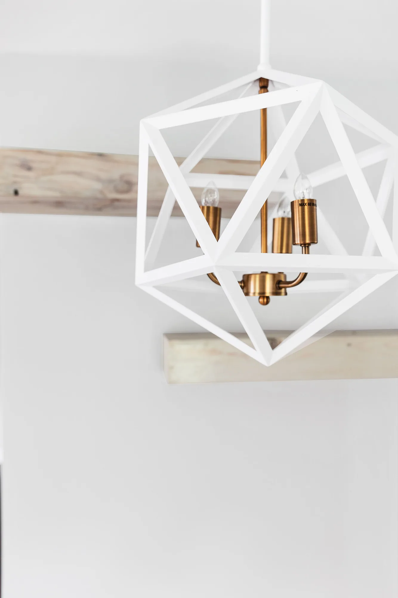 White geometric pendant with brass sockets below a wood beam