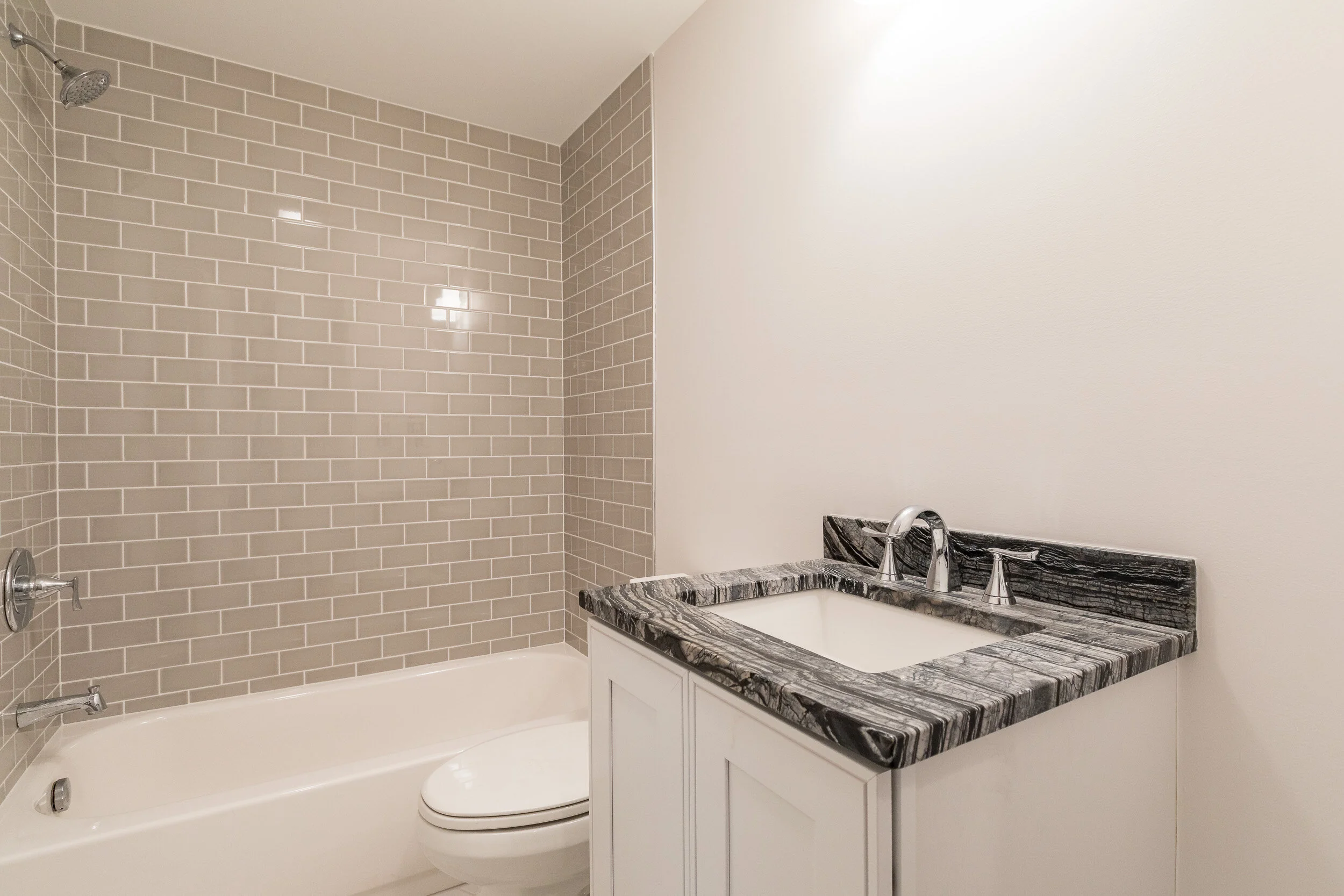 Bathroom with a gray subway-tile tub surround and a marble-topped vanity