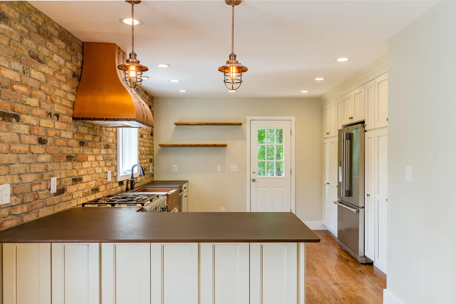 Country kitchen with an exposed brick wall, copper range hood, and open wood shelves