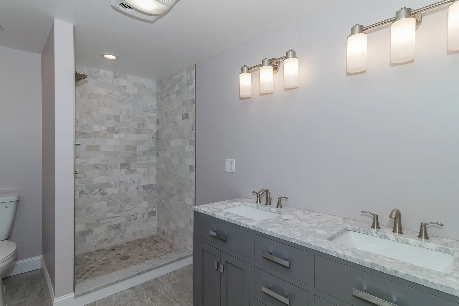 Spa bath with a gray vanity, marble counter, and sconces