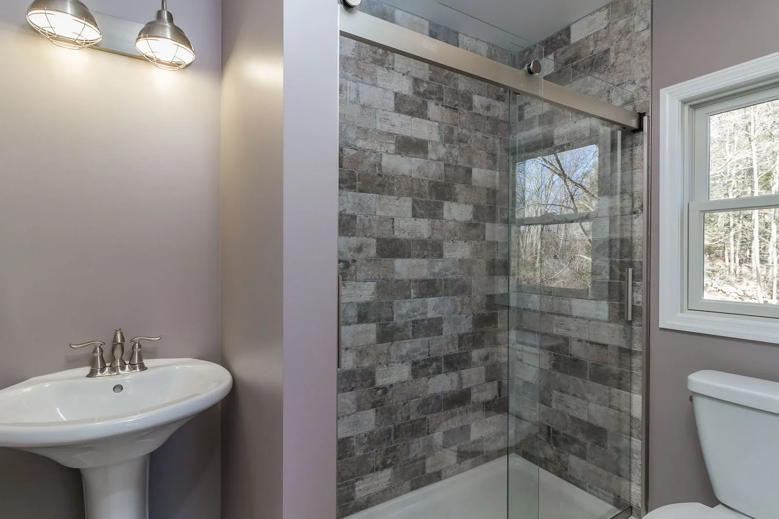 Glass shower with stacked stone tile beside a pedestal sink