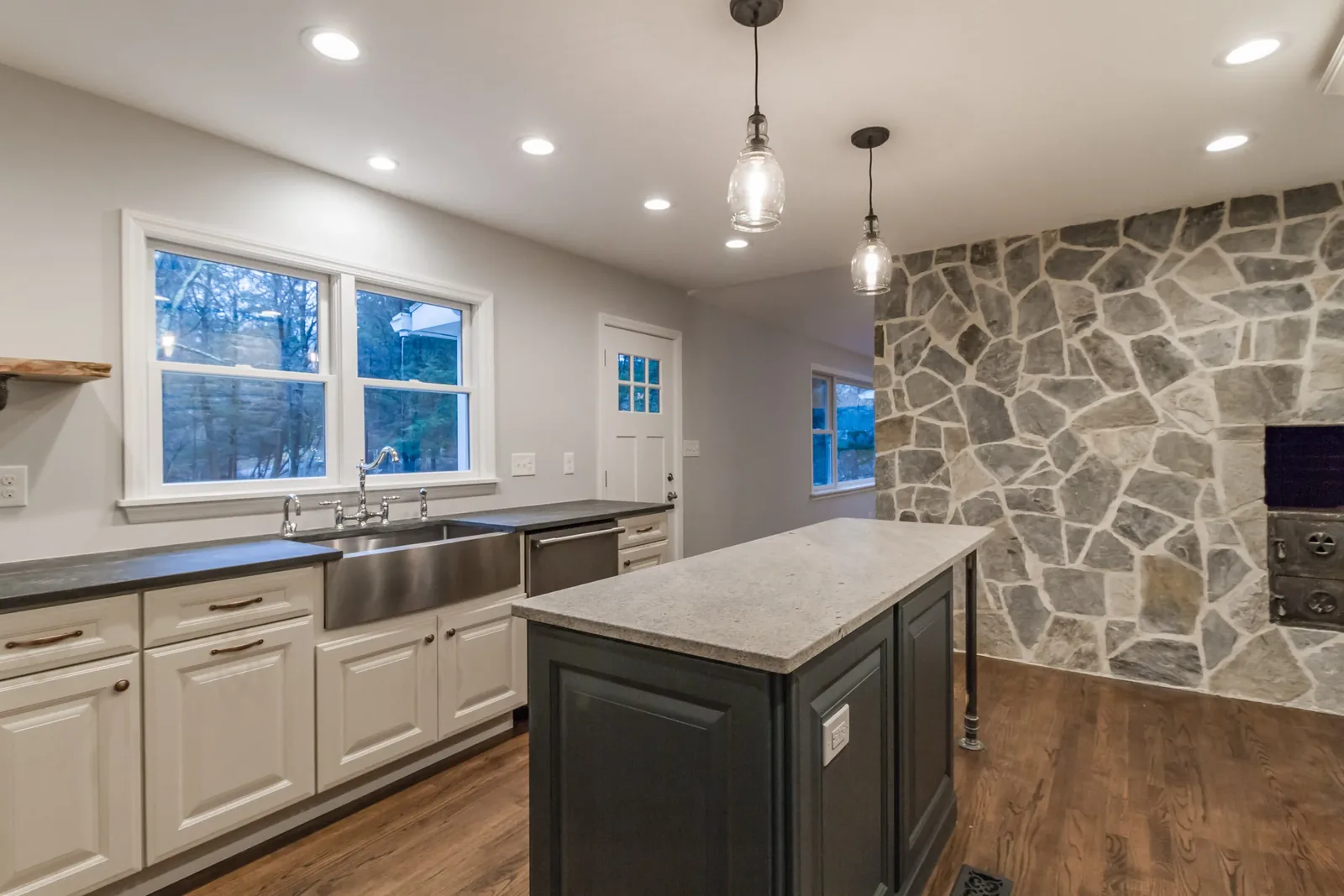 Kitchen with a stainless farm sink, stone accent wall, and soapstone island