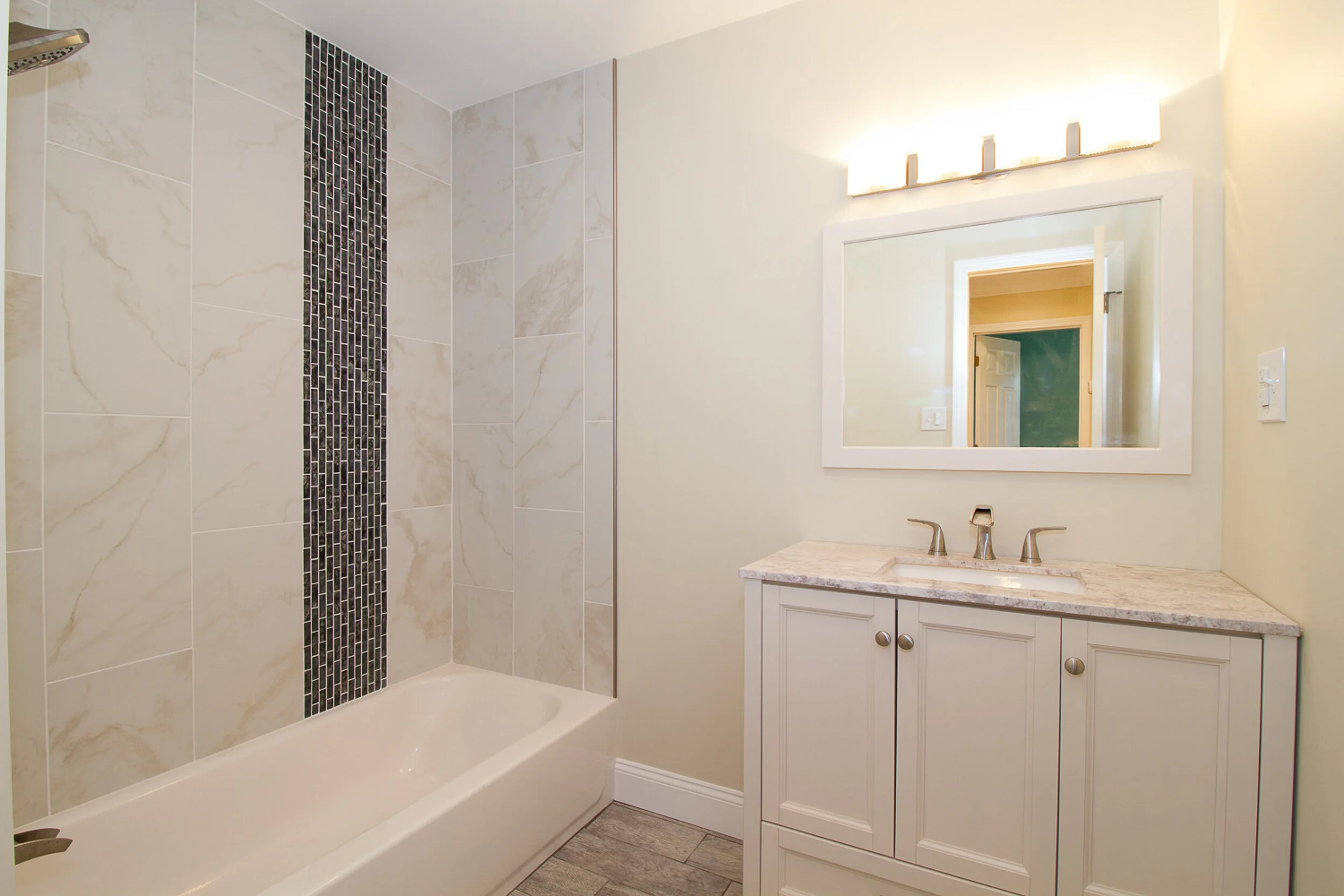 Bathroom with tub, marble-look tile, and mosaic accent band