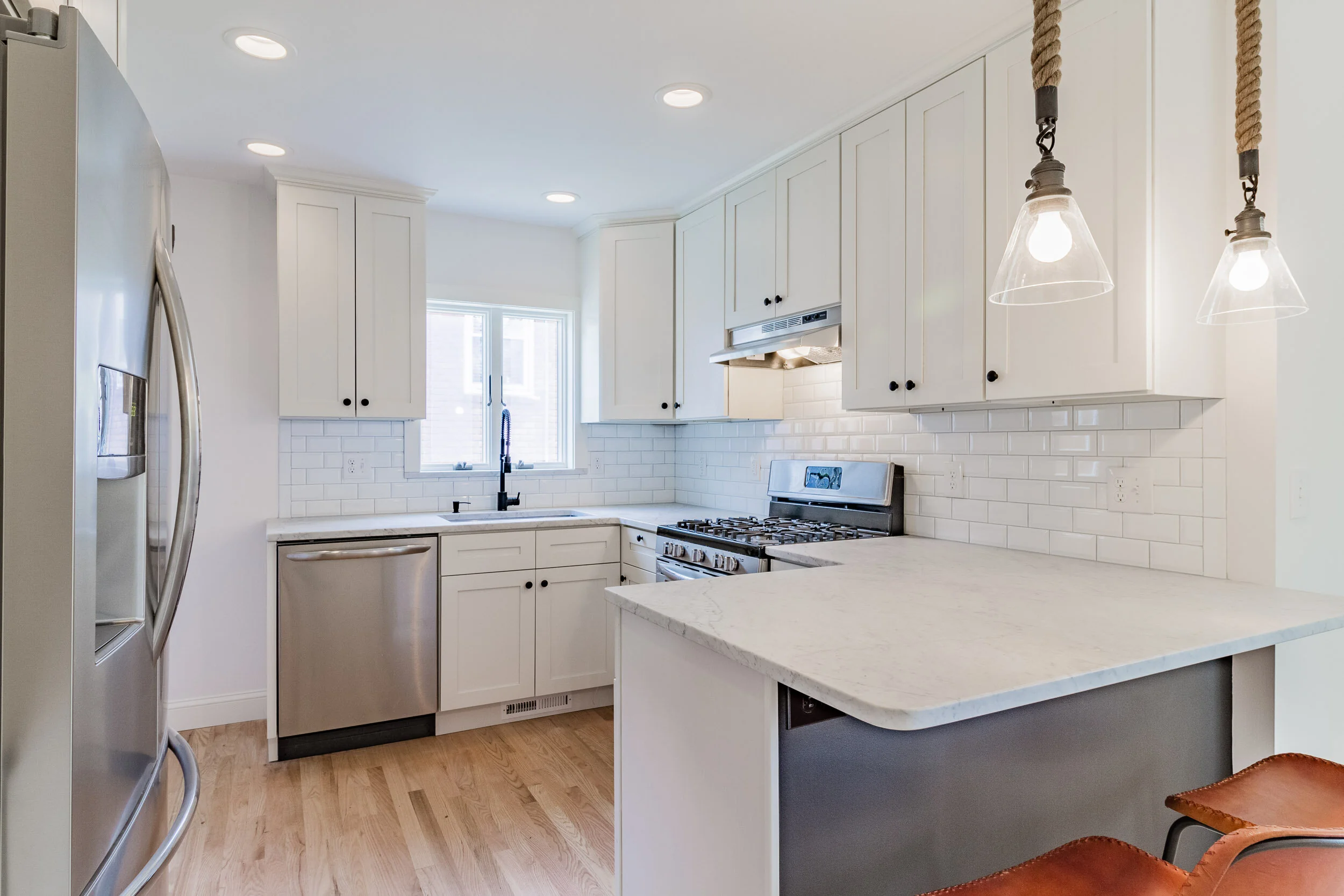 White kitchen with subway tile, marble counters, and rope pendants