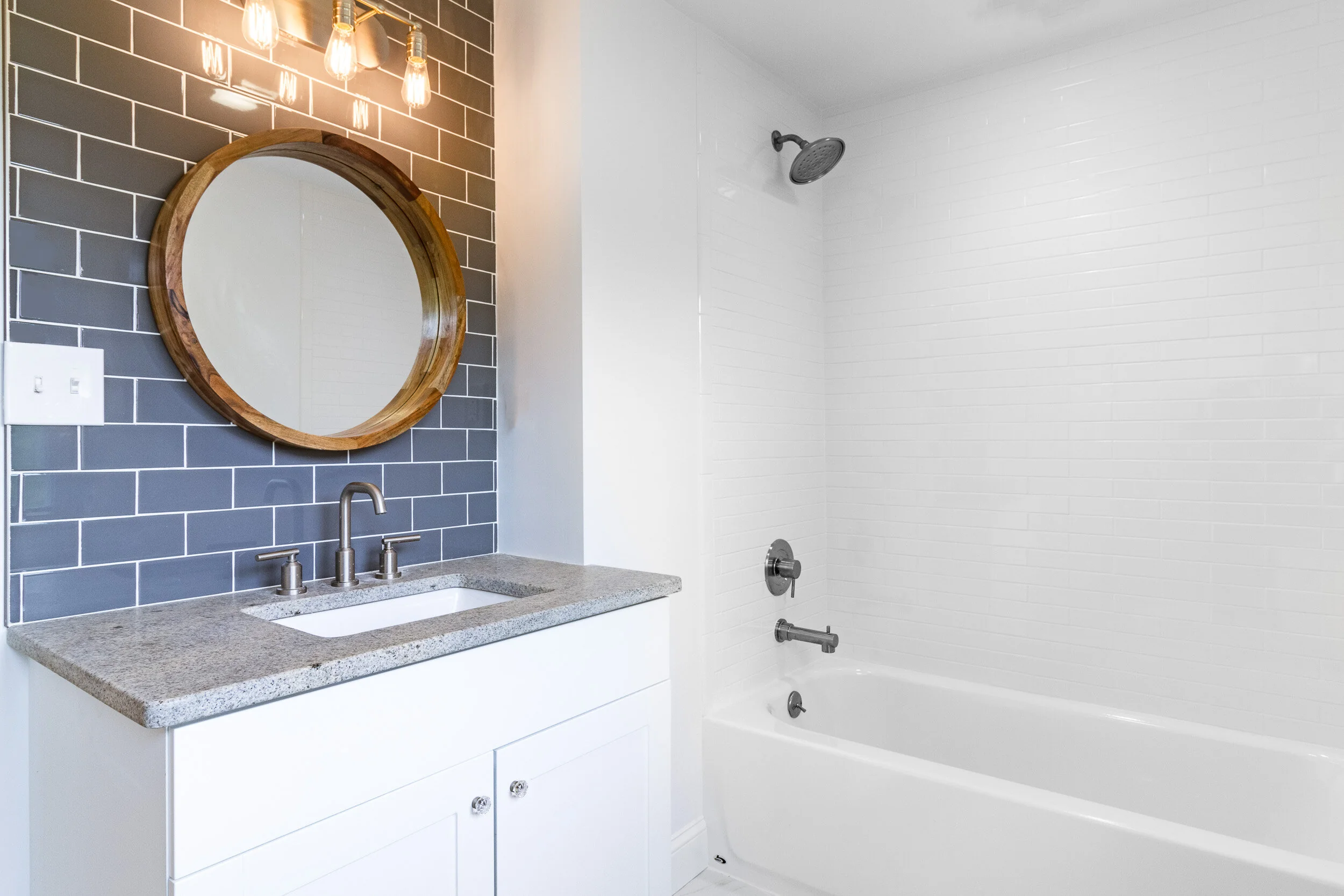 Bathroom with blue subway tile, granite vanity, and round wood mirror